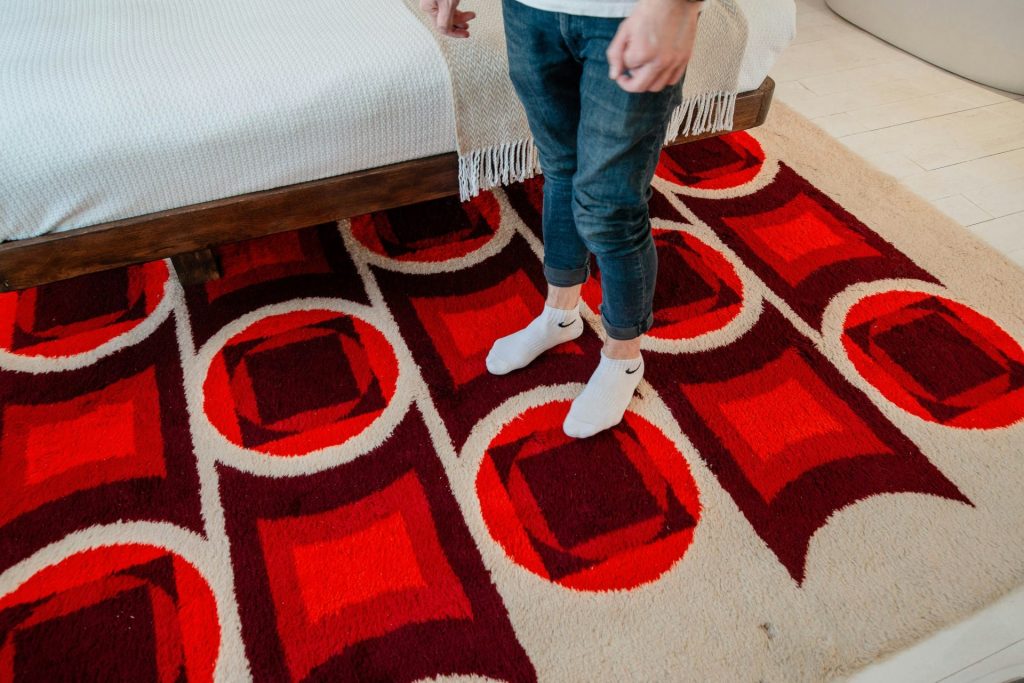 person in blue denim jeans and white sneakers standing on red and brown area rug